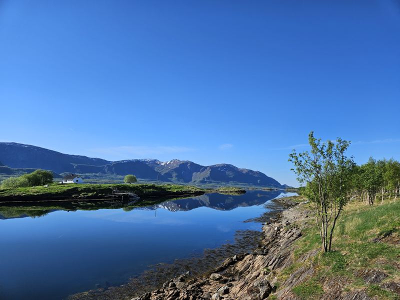Stille vann og fjell under blå himmel