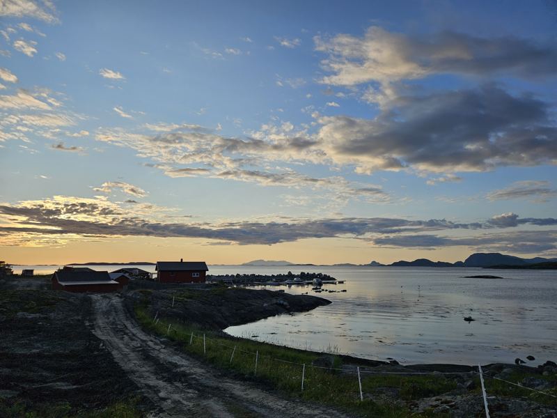 Solkveld over fjorden, med naust langs stranda
