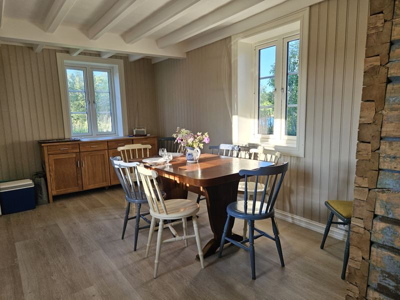 Spisestue med synlig tømmervegg og vinduer mot landskapet